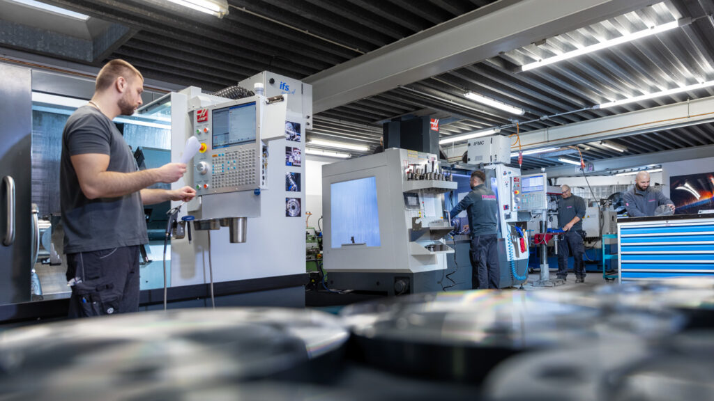 Produktion mit umfangreiche Bearbeitungsmöglichkeiten, von Aushalsen bis Zerspanen. Mitarbeiter stehen an unterschiedlichen Maschinen